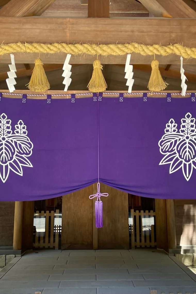 An entrance hung with a thick shimenawa rope above a purple curtain